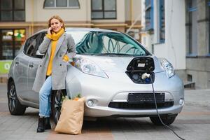 Woman with phone near an rental electric car. Vehicle charged at the charging station photo