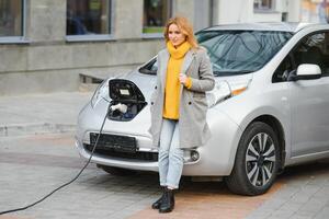 Woman with phone near an rental electric car. Vehicle charged at the charging station photo