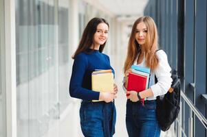 dos hembra estudiantes estar en el corredor de el Universidad con libros foto