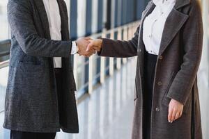 Business men and women shaking hands with a smile on the background of the large panoramic windows in a modern business center. Models dressed in a dark business suits. photo