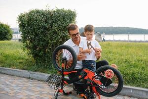 Happy father and his son having fun together at the green park, fixing bicycle together. father's day. photo