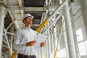 A young successful engineer with a drawing in his hands is standing in the territory of a modern factory. photo