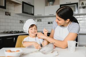 contento madre y su pequeño hijo sacudida crudo huevos en cuenco antes de haciendo masa para hecho en casa Pastelería en el cocina foto