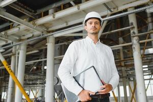 sonriente y contento empleado. industrial trabajador adentro en fábrica. joven técnico con blanco difícil sombrero. foto