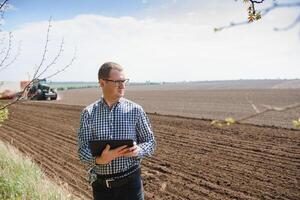 joven granjero en tierras de cultivo con tractor en antecedentes foto