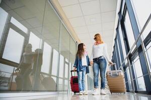 Beautiful mother and her stylish cute daughter walk together and pull a pink suitcase at airport. High season and vacation concept. Relax and lifestyles photo