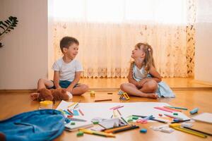 Kids drawing on floor on paper. Preschool boy and girl play on floor with educational toys - blocks, train, railroad, plane. Toys for preschool and kindergarten. Children at home or daycare photo