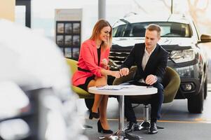 Car dealership sales person at work concept. Portrait of young sales representative wearing formal wear suit, showing vehicles at automobile exhibit center. Close up, copy space, background. photo