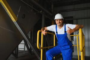 Young smiling professional in overalls and protective helmet standing in front of camera inside large machinebuilding plant photo