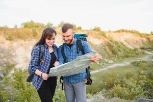 hermosa Pareja de un viajeros son buscando camino en ubicación mapa mientras en pie en alto colina en soleado día, masculino y hembra caminantes son caminando juntos en montañas durante largo esperando verano fin de semana foto