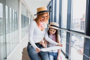 madre y pequeño hija con equipaje y mapa a aeropuerto terminal Listo para vacaciones. foto