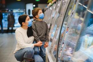 Mother and her son wearing protective face mask shop at a supermarket during the coronavirus epidemic. photo