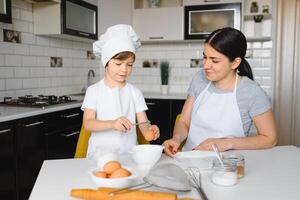 Happy mother and her little son shaking raw eggs in bowl before making dough for homemade pastry in the kitchen photo
