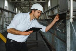 Close up of young Caucasian smiling worker with helmet on head using tablet for work while standing in warehouse. photo
