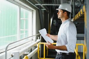 A young successful engineer with a drawing in his hands is standing in the territory of a modern factory. photo