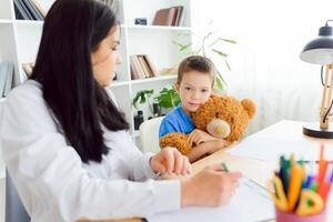 Female psychologist calming cute little boy in office photo