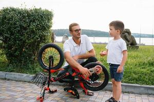 Happy father and his son having fun together at the green park, fixing bicycle together. father's day. photo