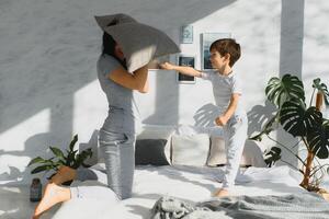 Mommy and son laughing and playing on the bed, having a pillow fight in the morning while wearing pajamas. Family casual lifestyle series. photo