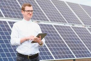 Portrait of man with a tablet in his hands standing near the solar panels station. Green ecological power energy generation. Solar station development concept. Home construction. photo