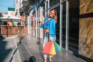 venta, consumismo, dinero y personas concepto - contento joven mujer con compras pantalones y crédito tarjeta en centro comercial foto