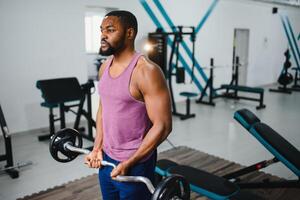 Concentrated African-American sportsman training bicep with heavy barbell in gym photo