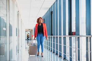 Full length side portrait of young black woman walking with suitcase in airport photo