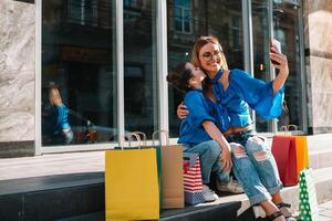 Young mother and her daughter doing shopping together. woman with girl child after shopping in street. woman with daughter with shopping bags outdoors. Woman and her daughter after shopping photo