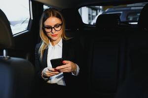 algunos ordenar de interesante información. inteligente mujer de negocios se sienta a asiento trasero de el lujo coche con negro interior. foto