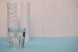 Water filters. Carbon cartridges and a glass on a white blue background. Household filtration system photo