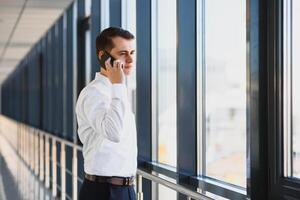Portrait of a serious confident man boss having mobile phone conversation while resting after meeting with his partners, businessman talking on cell telephone while standing in modern space indoors photo