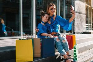 sale, consumerism and people concept - happy young women her dauther with shopping bags walking city street photo