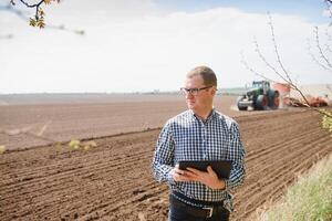 young farmer on farmland with tractor in background photo