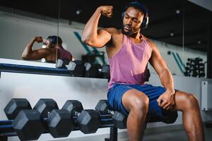 negro atleta flexionando músculos, demostrando fuerte bíceps en gimnasio foto