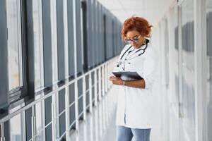 Portrait confident African American female doctor medical professional writing patient notes isolated on hospital clinic hallway windows background. Positive face expression photo