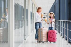 mujer con pequeño niña en internacional aeropuerto. madre con bebé esperando para su vuelo. hija con su madre comiendo plátanos de viaje con niños foto