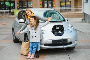 elegante madre y hija cargar un eléctrico auto, y gastar hora juntos. foto