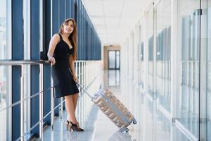 joven mujer con equipaje a el internacional aeropuerto. ella es muy contento de su vacaciones a calentar país en Navidad Días festivos foto