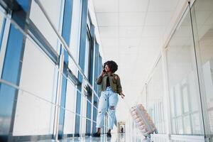 Full length side portrait of young black woman walking with suitcase in airport photo