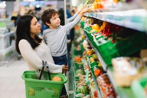 joven madre con su pequeño bebé chico a el supermercado. sano comiendo concepto foto