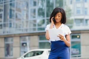 un bonito africano americano negocio mujer hablando en un célula teléfono a oficina edificio foto