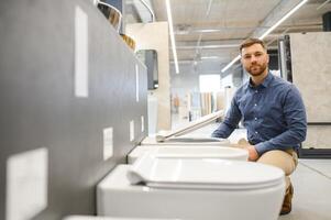 in a plumbing store, a man chooses a new toilet bowl photo