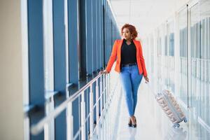 Young african american female passanger in casual clothes is in airport with baggage. photo