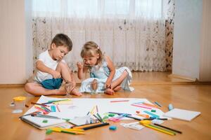 Kids drawing on floor on paper. Preschool boy and girl play on floor with educational toys - blocks, train, railroad, plane. Toys for preschool and kindergarten. Children at home or daycare. photo