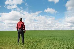 Young agronomist holds tablet touch pad computer in green wheat field. Agribusiness concept. agricultural engineer standing in a wheat field with a tablet in summer photo