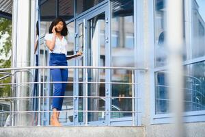 un bonito africano americano negocio mujer hablando en un célula teléfono a oficina edificio foto