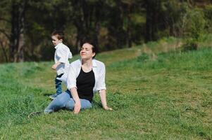 contento joven madre es jugando con su bebé en un parque en un verde césped. felicidad y armonía de familia vida. genial familia vacaciones. bueno fin de semana. madres día. día festivo. el concepto de un contento familia foto