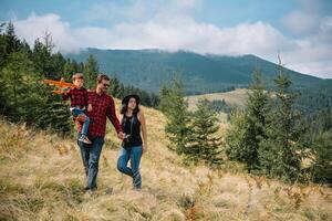 family walk on the field near the mountains in sunny day yellow grass father mother son holding hands on the sunset. photo