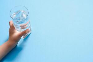 children's hand holding a glass of pure water on a blue background, copy space photo