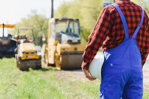 ingeniero pedidos para trabajadores a trabajo sin peligro a construcción sitio, trabajadores poner asfalto en el la carretera foto