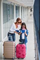 Mother and little daughter with luggage and boarding pass and passport at airport terminal ready for vacation. High season and vacation concept. Relax and lifestyles photo